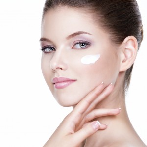 Beauty face of young woman with cosmetic cream on a cheek. Skin care concept. Closeup portrait isolated on white.